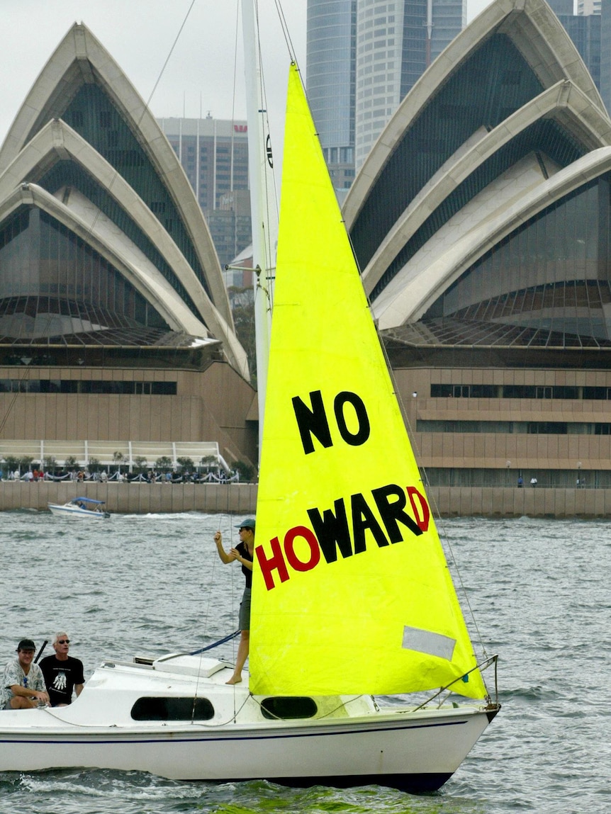A yacht with a no-war banner that reads "No Ho-WAR-d" floats past the Sydney Opera House, on the edge of the harbour.