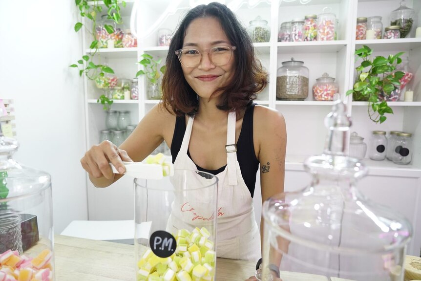A woman smiles while picking up lollies with tongs