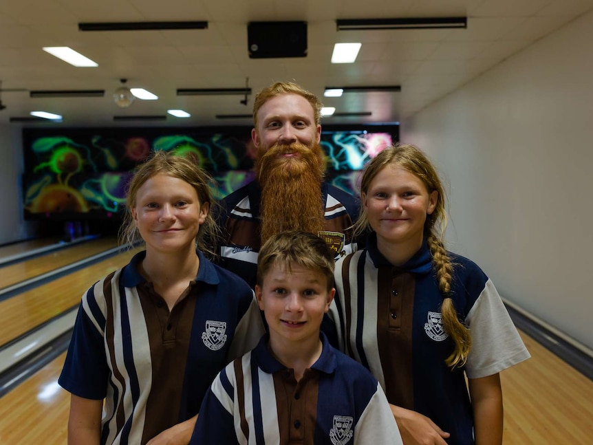 A teacher stands with three of his students standing in front of them. Neon coloured bowling alley in background. Ausnew Home Care, NDIS registered provider, My Aged Care