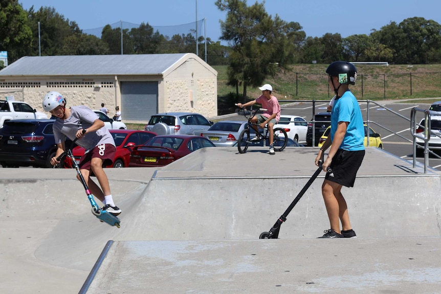 Young boys doing tricks at a skate park with their skateboards, scooters, and bicycles.