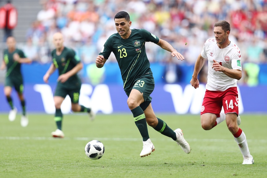Socceroos player Tom Rogic looks down as he runs with the ball at his feet during a World Cup game, with a defender chasing him.
