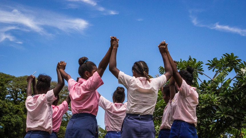 Girls in school uniform hold hands in triumph