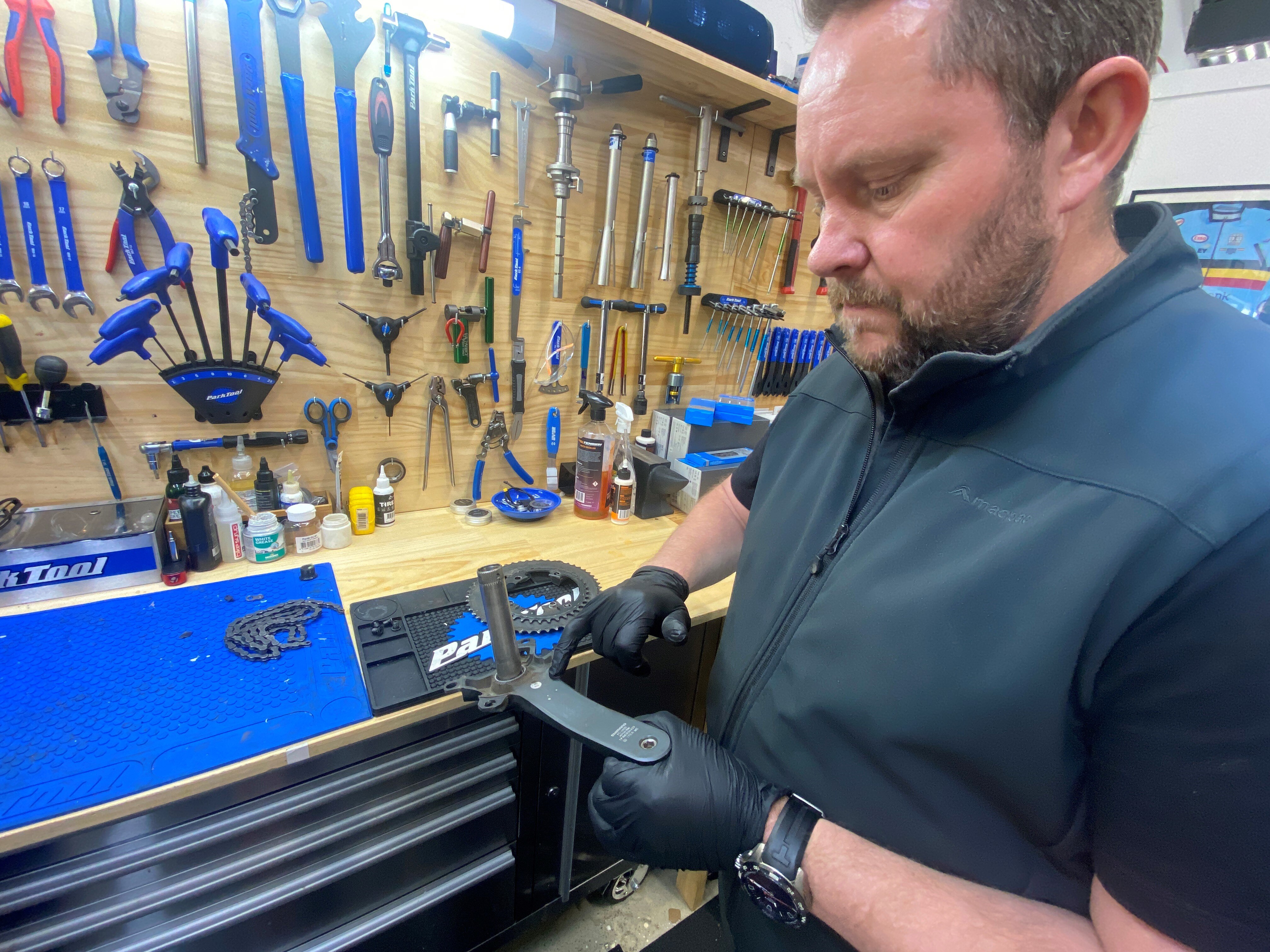 A man in a bike repair workshop holds a part in his latex gloved hand.