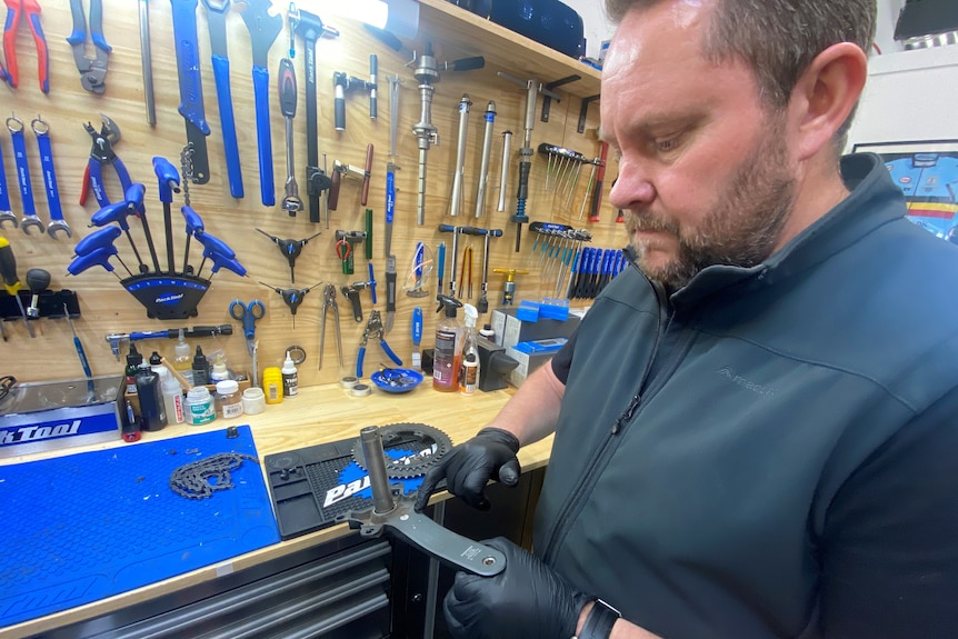 A man in a bike repair workshop holds a part in his latex gloved hand.