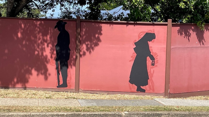 a red street divider wall with two silhouettes painted on it in black of a nurse and a soldier