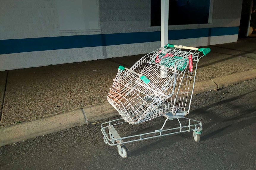 A mangled shopping trolley out the front of a shop on a dark street.