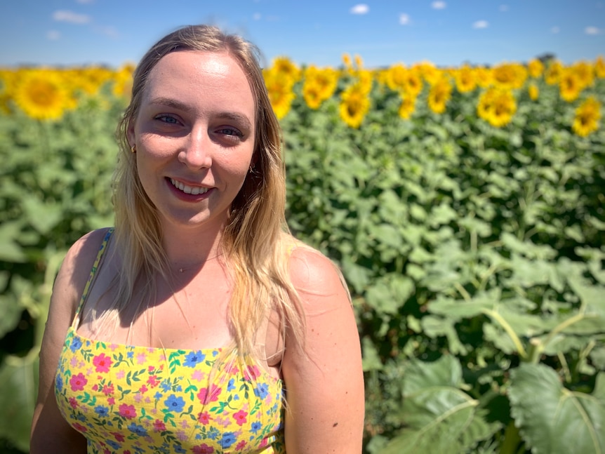 a woman in a yellow dress standing in front of sunflowers