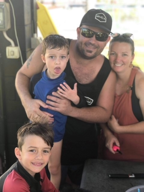 Four people look at the camera and smile. They are outdoors and wearing casual clothes. 