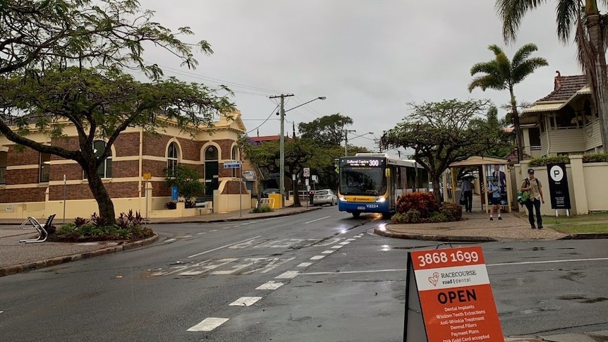A bus drives along Racecourse road, next to Kingsford Smith Drive, in grey and gloomy weather.