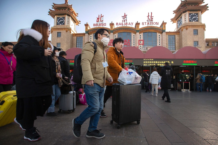 A traveller wears a face mask as he walks outside of the Beijing Railway Station with a crowd of people.