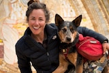 Adventurer Lucy Barnard smiling and dog Wombat looking at the camera holding an Ecuador sign