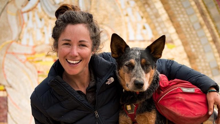 Adventurer Lucy Barnard smiling and dog Wombat looking at the camera holding an Ecuador sign