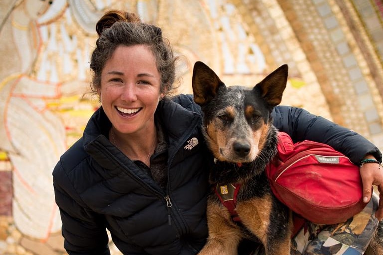 Adventurer Lucy Barnard smiling and dog Wombat looking at the camera holding an Ecuador sign