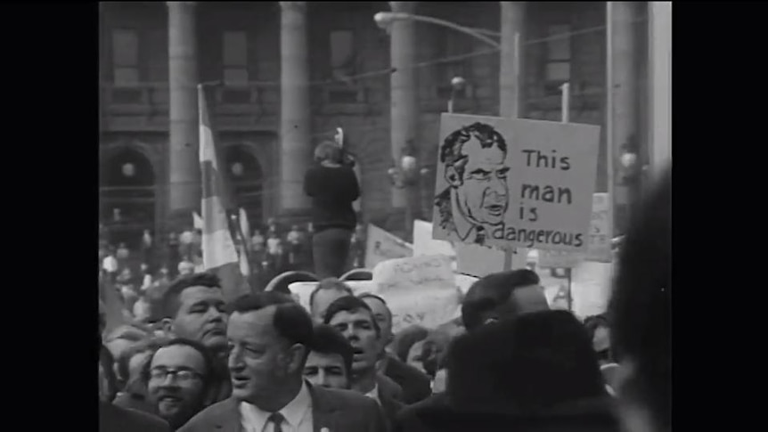 Old photo of protest crowd in street, sign of Nixon reads 'This man is dangerous'