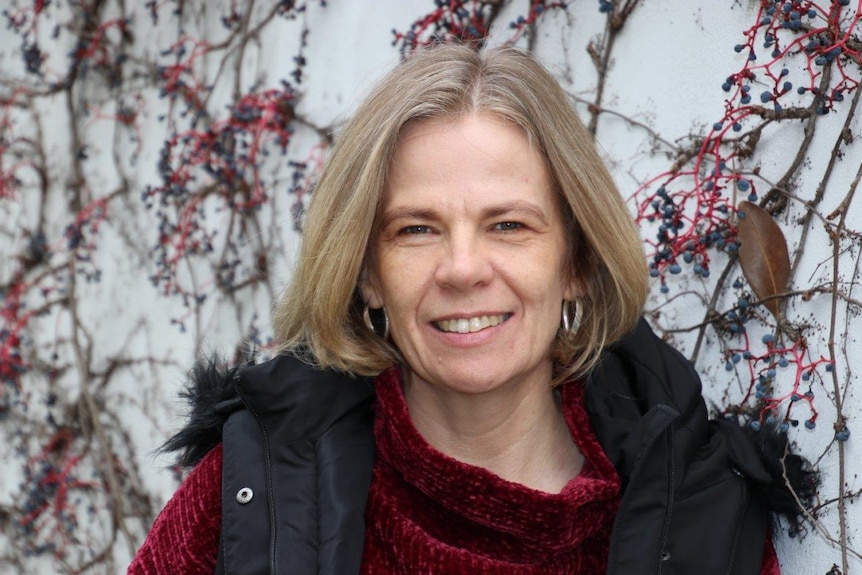 A smiling Helen Street stands in front of a wall with a red and black coloured creeping plant across it.