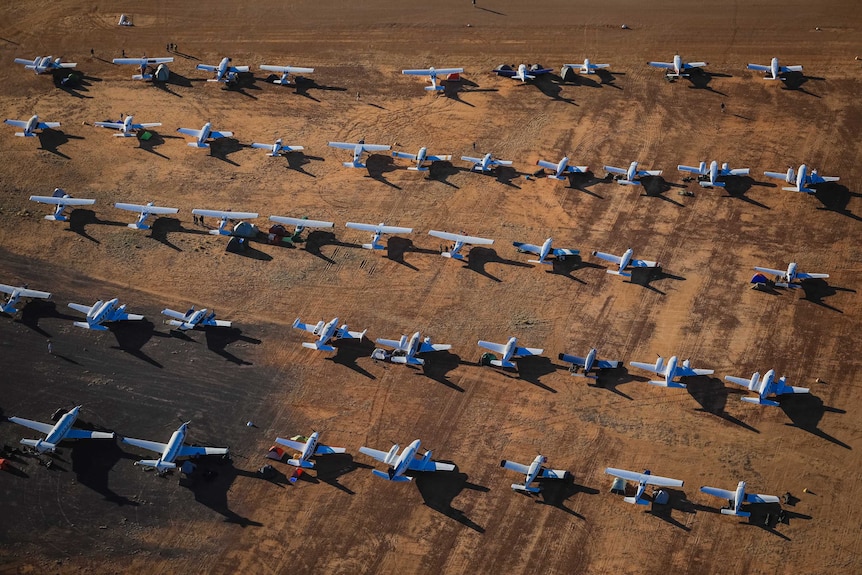 Aerial view of dozens of light planes lined up on the red dirt.