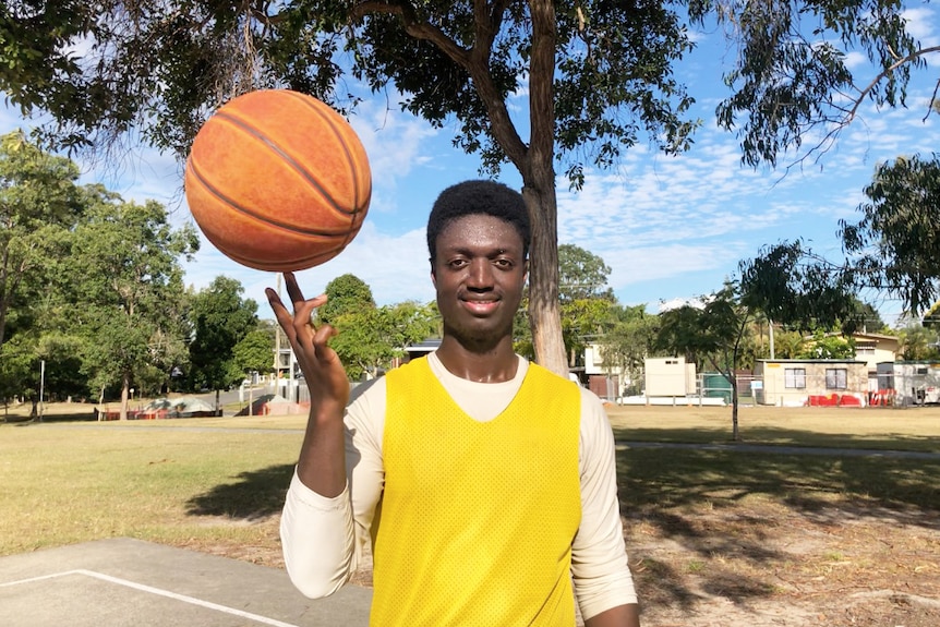 Basketball player Ali Sheriff balances a ball on his fingertips at a court in a park.