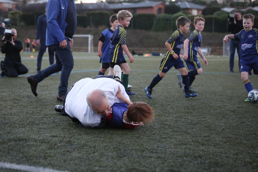 A grown man crashes into a child in a soccer pitch