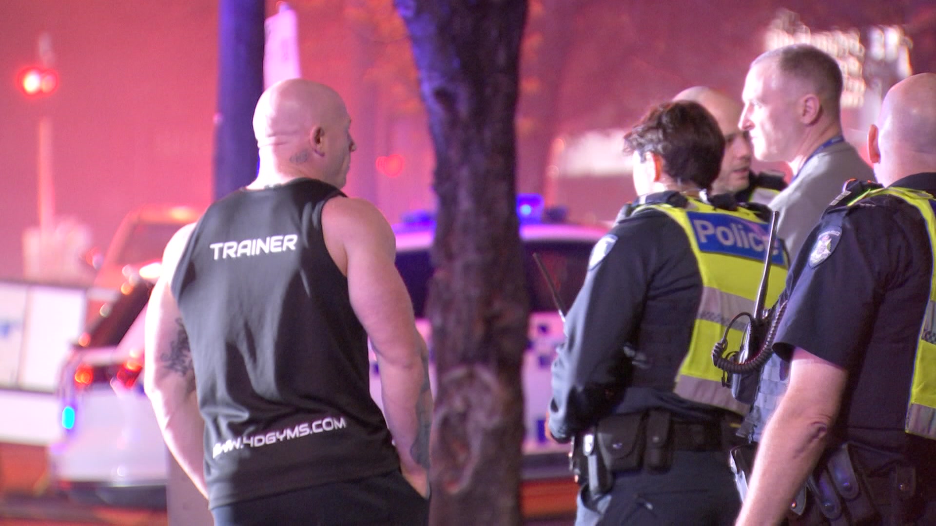 Police officers standing near a man in a gym singlet.