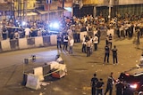 A wide view shows authorities keeping crowds of people back from the site of an explosion.