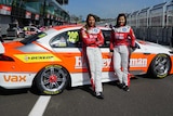 Two women dressed in racing gear stand in front of their Ford at the Mt Panorama race track.