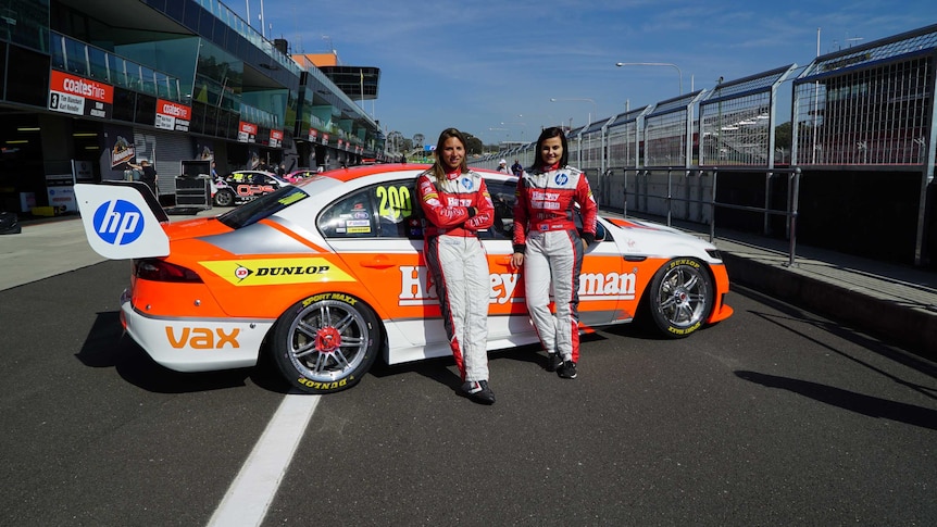 Two women dressed in racing gear stand in front of their Ford at the Mt Panorama race track.