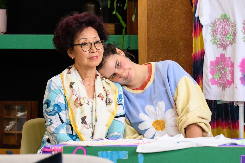 An older lady sits while a teenage girl rests her head on the lady's shoulder