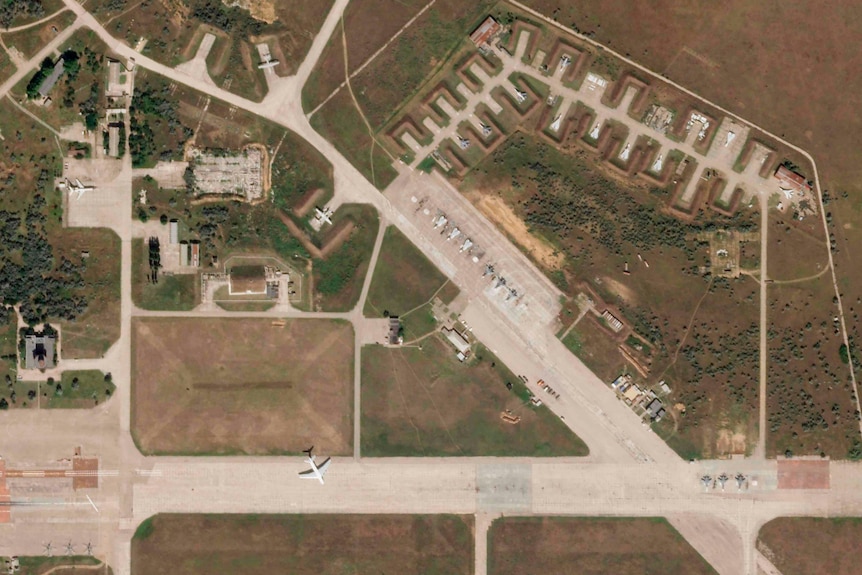 A satellite image shows white aircraft parked on grey concrete bays in a green outdoor area.