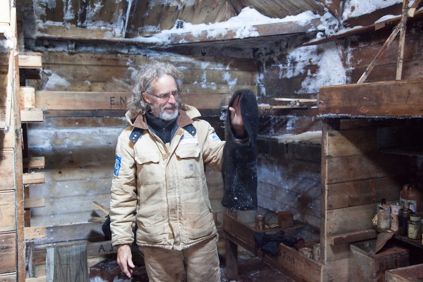 Dr Ian Godfrey inside the hut holding a piece of clothing