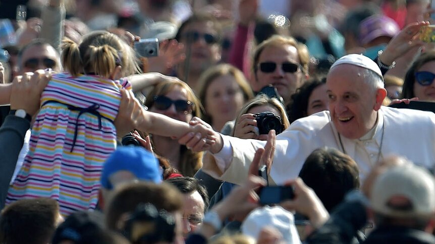 Pope Francis shakes the hand of a child in a crowded at St Peter's square