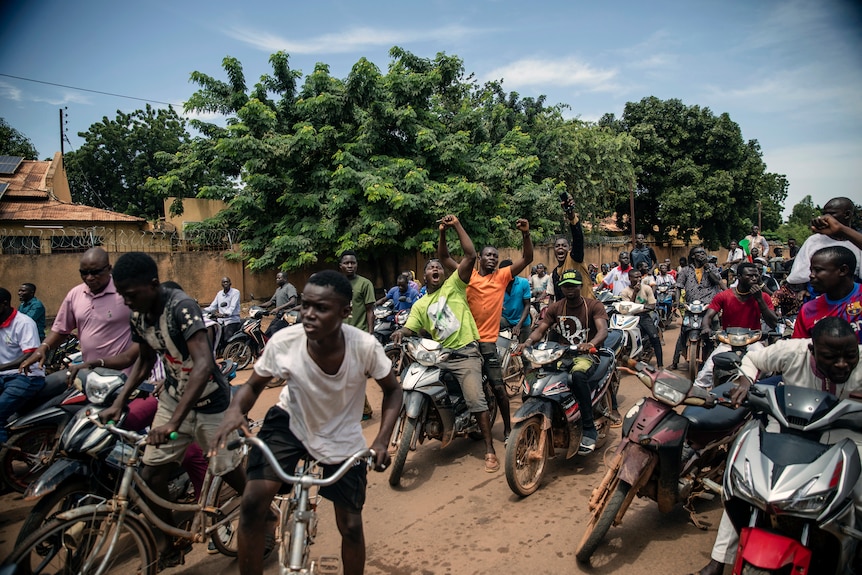 Protestors on the steet, fists in the air, shouting, while sitting on bicycles and scooters.