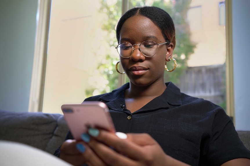 Angelica Ojinnaka sits on a sofa and looks down at her phone