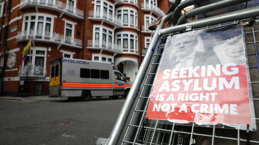 A poster saying "Seeking asylum is a right not a crime" is attached to a barrier across from the Ecuadorian Embassy in London.
