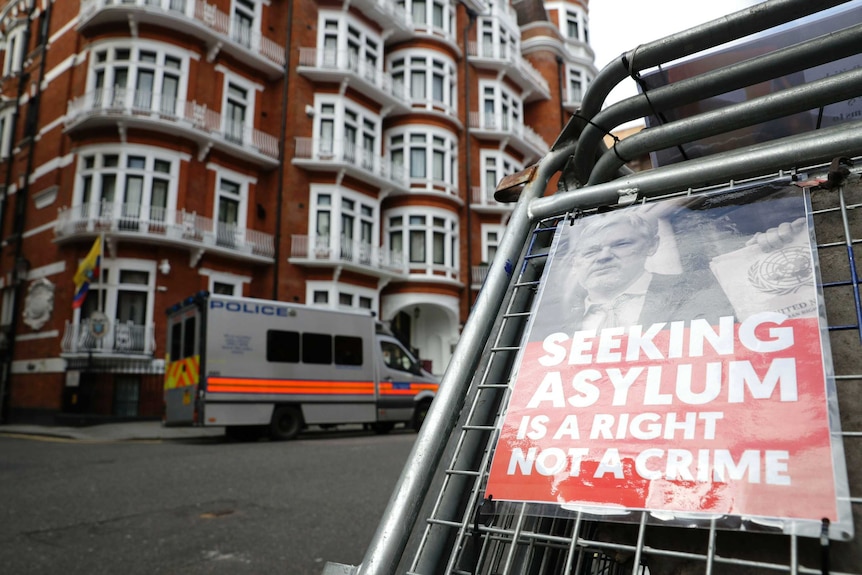 A poster saying "Seeking asylum is a right not a crime" is attached to a barrier across from the Ecuadorian Embassy in London.