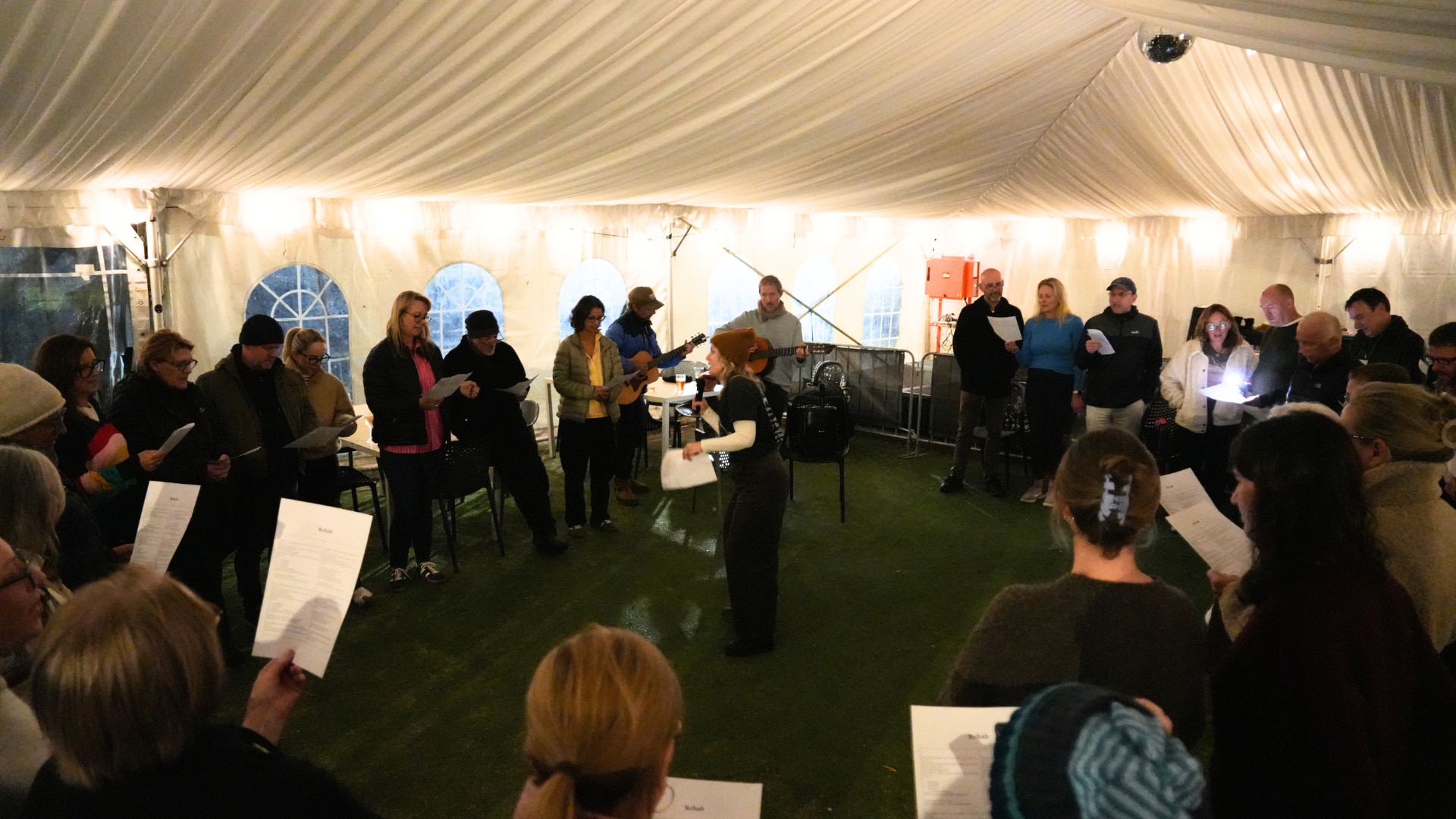 A woman is standing in the middle of a circle, with a microphone in hand as she teaches a group of people to sing.