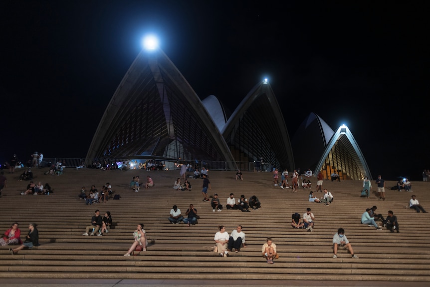 Groups of people sit apart from each other on the steps to the Sydney Opera House