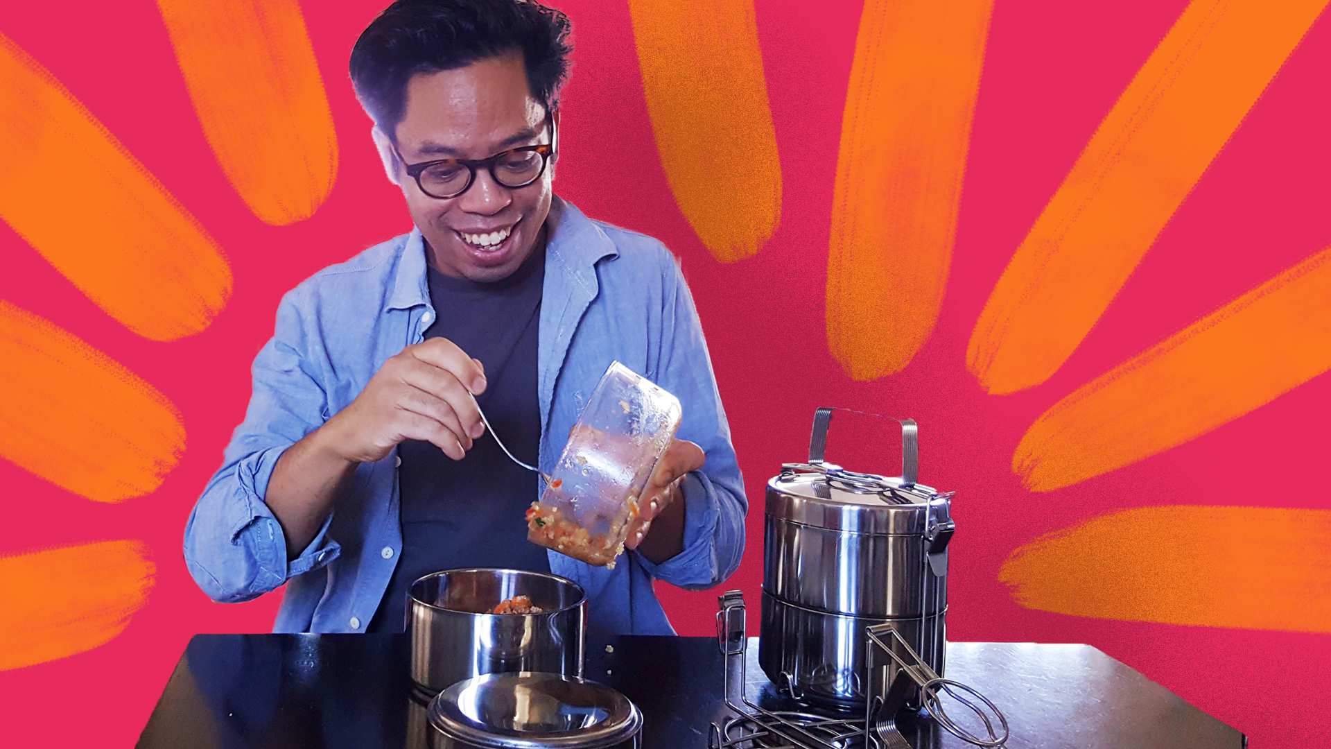 A man smiling while putting salad from a glass bowl into a metal tiffin