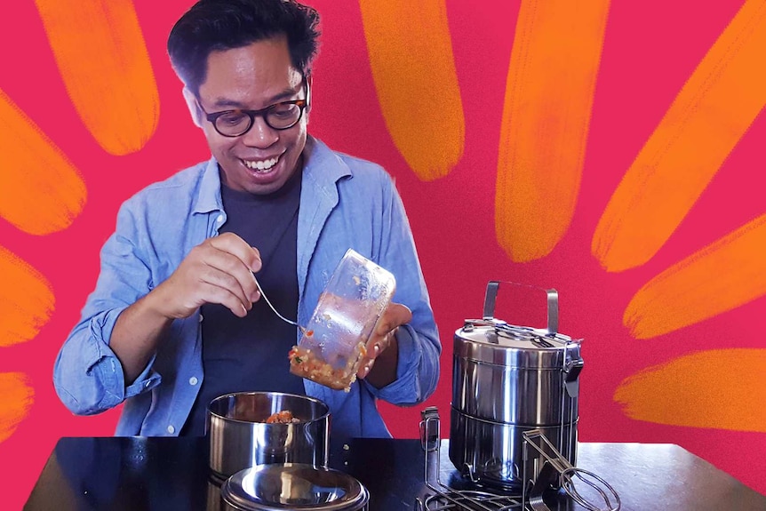 A man smiling while putting salad from a glass bowl into a metal tiffin