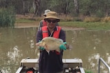 a man wearing green gloves holds a golden perch on a boat in a river