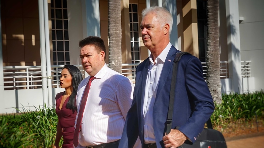 John McRoberts and his lawyer Anthony Elliot walk outside court with a woman. The sun casts tree's shadows onto buildings