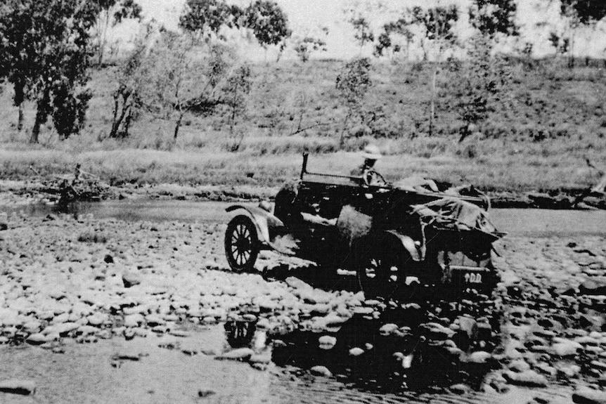 An archival black and white photo of a Model T Ford crossing a river bed in 1919.