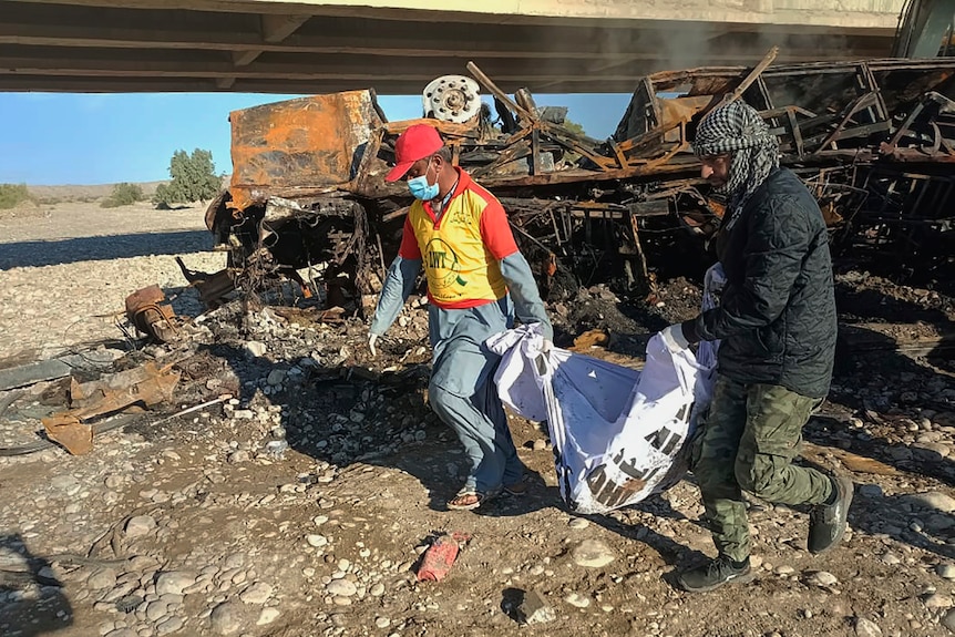 Two rescue workers are pictured collecting remains from the burnt wreckage of a bus accident.