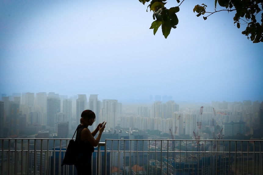 An unidentifiable woman stands at a railing overlooking the Singaporean skyline