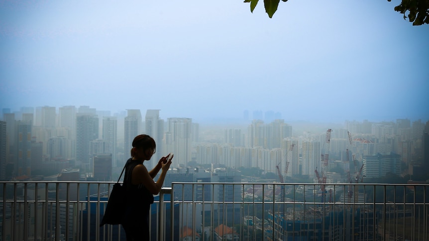 An unidentifiable woman stands at a railing overlooking the Singaporean skyline