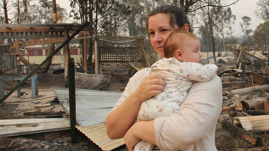 A woman and a baby in front of a destroyed property pictured in story about bushfire trauma.