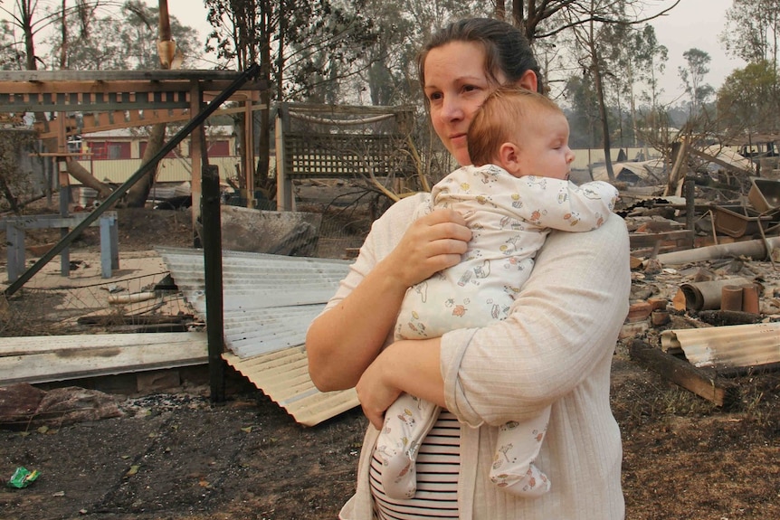 A woman and a baby in front of a destroyed property
