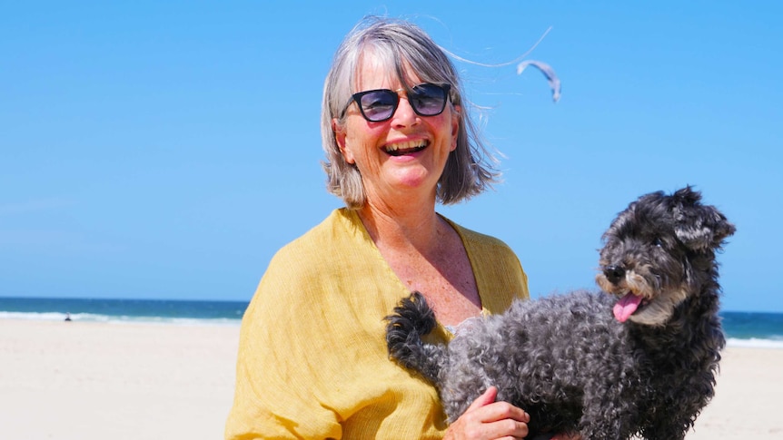 A woman with her dog on a beach in the sunshine