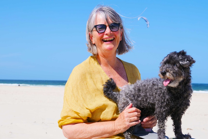 A woman with her dog on a beach in the sunshine