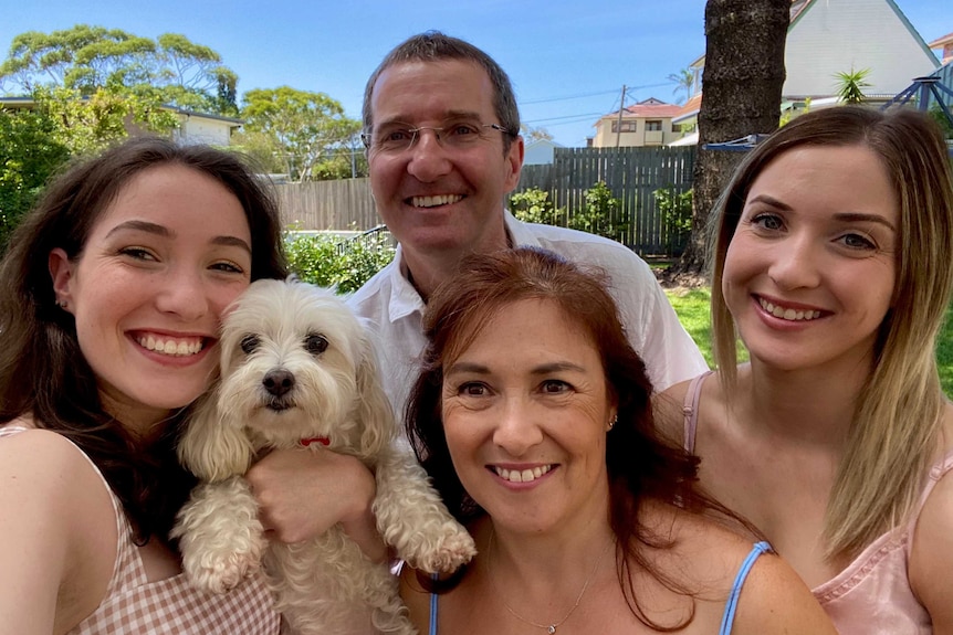 Three woman and one man smile at the camera. One woman holds a small dog.