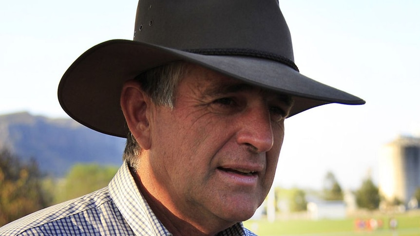 John Anderson, wearing an Akubra hat and checked shirt, stands on a farm